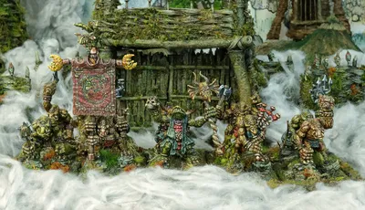 A group of intricately detailed miniatures inspired by Celtic mythology is displayed in front of a rustic, weathered structure covered in moss and foliage. The miniatures, depicting various fantastical creatures, include a central figure holding a banner, flanked by others wielding weapons and adorned with unique features like tusks and intricate patterns. The scene is set amidst a misty, ethereal atmosphere, enhancing the mystical theme of the Famhairean campaign.