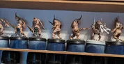 Four miniature figures on round bases, posed in combat stance. Leftmost figure has curved horns, a tusk, and a weapon in one hand. Second figure has a blue gem on its forehead, wielding a club. Third figure holds a large sword and shield. Fourth figure has a multi-pronged weapon.