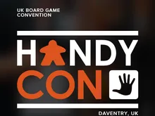 White text on dark background reads "UK BOARD GAME CONVENTION." Large orange and white text spells "HANDYCON" with an orange icon of a person in a wheelchair between letters. To the right, an orange hand icon. Small white text at bottom reads "DAVENTRY, UK."