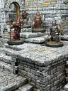 A detailed scene showcases a modular dungeon setup made from intricately sculpted stone blocks, featuring various levels and staircases. Four miniatures are positioned on the blocks: a bearded wizard with a staff, a robed figure holding a spear, and a knight in armor wielding a weapon, all engaged in exploration. The textured stone surfaces and the overall layout highlight the versatility of the dungeon blocks for tabletop gaming.