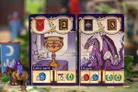 Two game cards from Greylune. Left card shows a golden chalice labeled "Calice sacré" with a red shield emblem, number 2, and icons for 5 blue, 4 green, and 4 gold tokens.