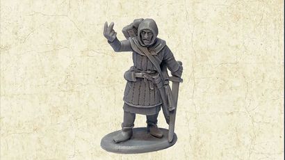 A grey resin miniature of the Master Fletcher stands on a circular base, depicted in a friendly pose with one hand raised in a gesture. He is dressed in a hooded cloak and tunic, with a quiver of arrows slung over his shoulder and a sword at his side. The background features a textured, light-colored surface that enhances the focus on the figure.