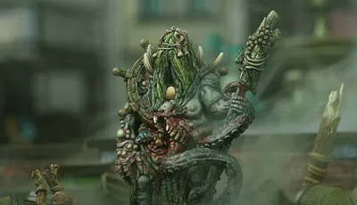Green-skinned monster with long hair, horns, and a staff, holding a severed head.