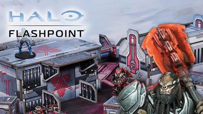 A detailed gaming scene from Halo: Flashpoint features a futuristic battlefield with intricately designed terrain and structures. In the foreground, a blue-armored character stands on a raised platform, while two red-armored figures engage in action nearby. The backdrop showcases a variety of buildings with sci-fi elements, emphasizing the game's immersive environment. The title "HALO FLASHPOINT" is prominently displayed at the top.