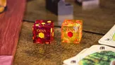 Two translucent dice with "CATAN" text and colored internal shapes on a dark surface.