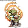 A green, serpentine miniature figure with a large, open mouth and visible teeth, surrounded by a circular arrangement of orange and red flame-like elements with brown wooden debris. The figure is coiled around a small, detailed structure resembling a chimney with a colorful, striped umbrella attached. The base is textured with gray rubble. Text at the top reads: "MINIATURES ARE SUPPLIED UNASSEMBLED AND UNPAINTED". Text at the bottom reads: "©2026 MARVEL © AMG".