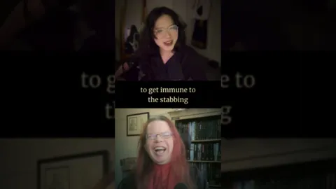 Two individuals are engaged in a lively conversation, with one person on the top half of the image and the other on the bottom. The person at the top has dark, wavy hair and is wearing glasses, while the person at the bottom has long, reddish hair and is also wearing glasses. The background features shelves filled with books and other items, suggesting a cozy, personal space. Subtitles appear on the screen, with the phrase "to get immune to the stabbing" prominently displayed, adding a humorous and intriguing context to their discussion.