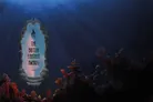 A stylized underwater scene features a large, ornate mirror framed in coral and seaweed, with the text "THE BRITISH FANTASY AWARDS 2022" prominently displayed in the center. The background is a deep blue, suggesting depth and mystery, with rays of light filtering through the water above. Colorful coral formations in shades of orange, pink, and purple surround the mirror, enhancing the fantastical underwater theme.