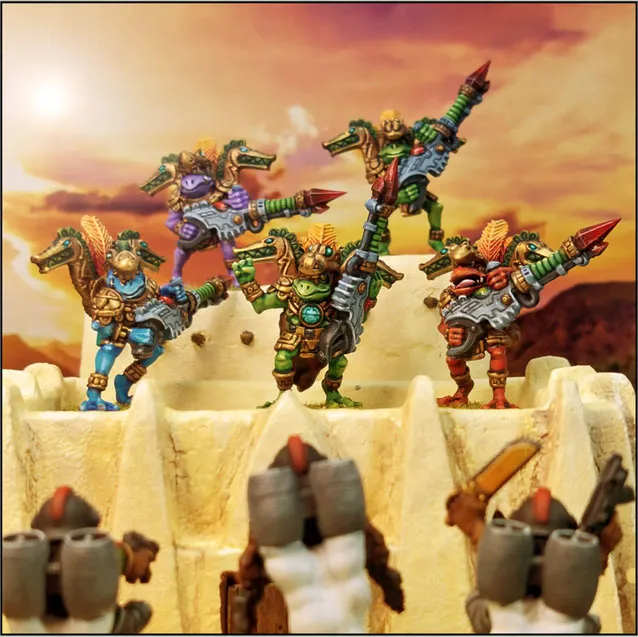 A group of colorful Space Frogmen miniatures stands atop a sandy, fortress-like structure, each wielding futuristic weapons. The frogmen are adorned in vibrant armor, featuring hues of blue, green, purple, and red, with intricate details like feathers and mechanical elements. In the foreground, two additional frogmen are partially visible, facing away from the viewer, suggesting a larger scene of camaraderie or preparation for battle against a dramatic sunset backdrop.