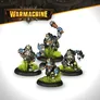 A group of four trollkin figures from the Southern Kriels Kithguard army for Warmachine, each standing on round black bases adorned with tufts of green grass. The figures are dressed in rugged, dark clothing with mechanical elements, featuring distinctive masks and goggles. One figure is raising a weapon, while the others are posed in various stances, showcasing their unique designs and expressions.
