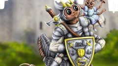 A whimsical illustration features a large, anthropomorphic creature resembling a knight, complete with armor and a crown, holding a shield adorned with a castle emblem. Perched on its shoulder is a smaller creature dressed in blue, while a tiny dragon-like figure stands beside them, also in armor. The background showcases a blurred castle and green grass, creating a playful and fantastical atmosphere.