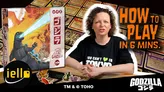 A woman with curly hair is seated in the foreground, wearing a black t-shirt that reads "YOU CAN'T ♥ IN TOKYO." Behind her, a colorful array of game cards is visible, featuring various designs and symbols related to the game. The box for "King of Tokyo Godzilla" is positioned to the left, and the text "HOW TO PLAY IN 6 MINUTES" is prominently displayed above her.