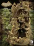 Miniature stone tower with crumbling walls, arched doorway, and moss-covered base. Surrounding terrain includes rocky ground, trees, and distant miniature figures. Logo in bottom right corner reads "Hagglethorn Hollow Hobbies."