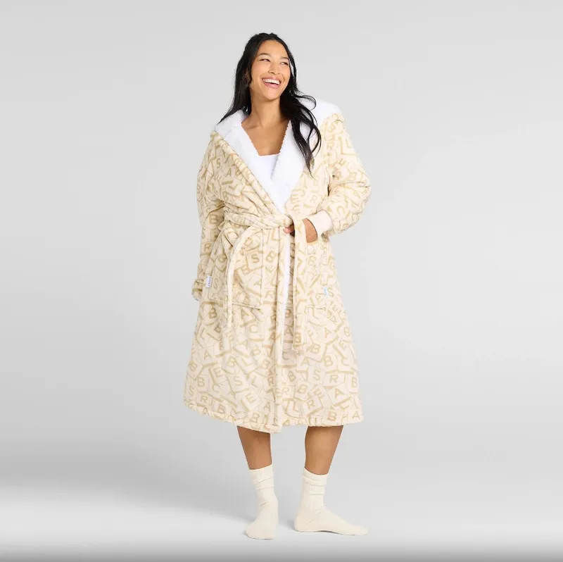 Woman in long cream robe with Scrabble tile pattern, white socks, smiling.