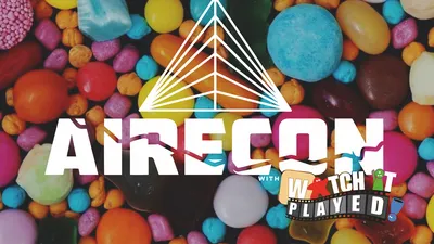 A colorful assortment of candies in various shapes and sizes serves as the backdrop for the event branding. The word "RECON" is prominently displayed in bold white letters, with a stylized triangular logo above it. Below, the text "with WATCH PLAYED" is featured in a playful font, suggesting a fun and engaging gaming event.
