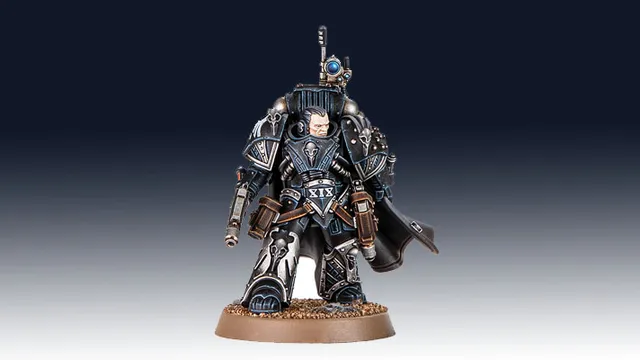 Kaedes Nex, the Moritat-Prime of the Raven Guard, stands prominently in the image, showcasing intricate details in his armor. He is clad in dark, metallic blue and silver, with a flowing black cape and various pouches and weapons attached to his belt. His helmet features a distinctive design, and he holds a weapon in one hand, while a small device is mounted on his shoulder, emphasizing his role in covert operations. The base is textured with a sandy finish, enhancing the overall presentation of this formidable character.