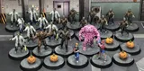 A collection of 30mm scale resin miniatures from the "Monsters Invaded My Town" set features various characters, including 16 zombies, a Frankenstein figure, a Sludge creature, a Werewolf, and two heroes. The scene includes five pumpkin spawn points, with the miniatures displayed on 32mm black plastic bases. The background shows a stylized urban environment, enhancing the thematic elements of the game.