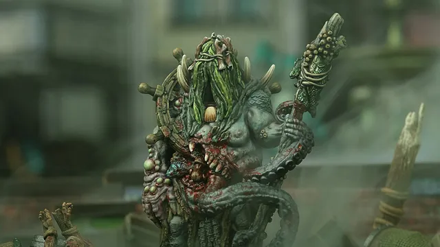 Green-skinned monster with long hair, horns, and a staff, holding a severed head.