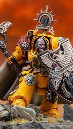 A dynamic miniature of Darnath Lysander in bright yellow Terminator armour, holding the relic storm shield Rampart in one hand and the Fist of Dorn power hammer in the other. His expression is fierce, and he wears a flowing cape, with intricate details on his armour and shield, including the name "LYSANDER" and various symbols. The background features a dramatic, fiery sky, enhancing the imposing presence of the character.
