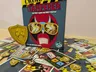 Crime Scene Tamperer game box with cards and tokens scattered on a wooden floor.