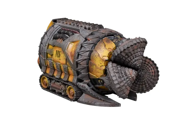 A rugged, heavily-armored vehicle resembling a tunneling machine, featuring a large, spiked front and a cylindrical body with various mechanical details. The surface is painted in shades of yellow and brown, with weathered textures that suggest heavy use. The rear of the vehicle has a series of tracks, indicating its capability to navigate through rough terrain.