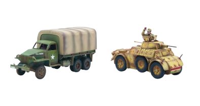 A green and brown camouflaged American Studebaker truck is positioned on the left, featuring a covered cargo area and a white star insignia on its side. Next to it, on the right, is a tan Autoblinda AB41 armored car, showcasing a rounded body and a turret, with a slightly weathered appearance. Both vehicles are detailed models suitable for tabletop gaming, reflecting their historical designs from WWII.