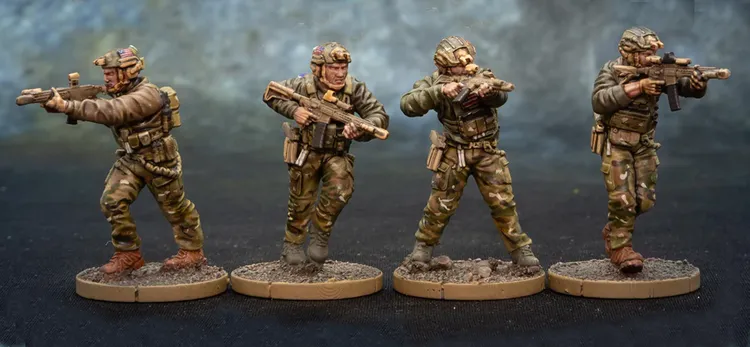 Three detailed miniature figures of soldiers are displayed, each standing on a circular base with a textured surface resembling dirt. The figures are dressed in tactical gear with camouflage patterns, holding various firearms. The soldier on the left is aiming a rifle, the central figure is preparing to fire, and the soldier on the right is also holding a weapon, showcasing a variety of poses and expressions that convey action and readiness.