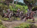 Three halfling cavalry figures are riding horses through a lush, green landscape. Each rider is equipped with different weapons: one holds a spear, another has a javelin, and the third carries a lance. The horses are adorned with saddles and gear, and the background features dense foliage and trees, enhancing the natural setting.