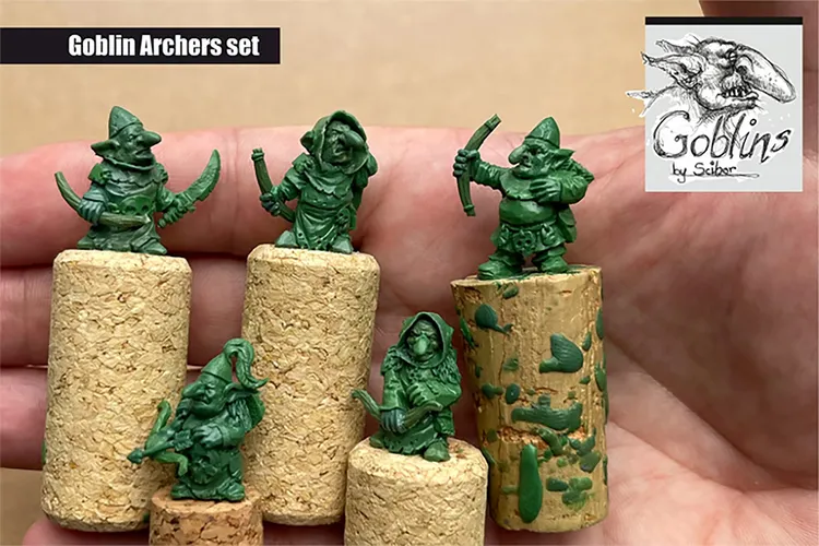 A set of five green goblin archer miniatures is displayed on cork bases, showcasing their unique designs and poses. Each goblin features distinct characteristics, such as pointed hats and various weapons, emphasizing their mischievous nature. The background is neutral, allowing the vibrant green of the miniatures to stand out prominently.
