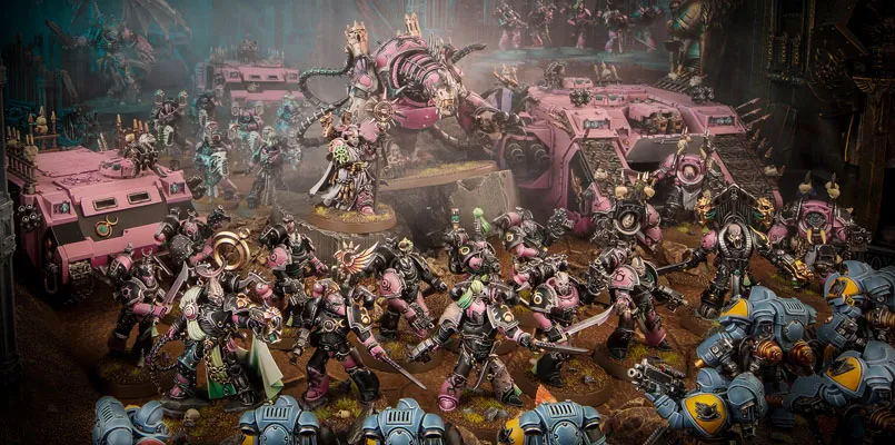 The image features a dynamic scene filled with a multitude of Emperor’s Children miniatures from the Warhammer 40,000 universe, showcasing their vibrant pink and purple color scheme. In the foreground, a diverse array of Chaos Space Marines, adorned with ornate armor and chaotic symbols, engage in battle, while a towering, menacing figure looms behind them, possibly a Daemon Engine or a warlord. Several vehicles, including armored transports, are also present, adding to the chaotic atmosphere of the battlefield, which is set against a dark, atmospheric backdrop. The overall composition emphasizes the flamboyant and hedonistic nature of the Emperor’s Children, reflecting their devotion to Slaanesh.