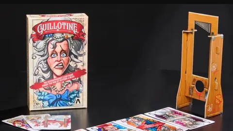 The image features the box of the card game "Guillotine," prominently displaying an illustration of a startled woman with gray hair and a blue bow, set against a light-colored background. Next to the box, a wooden guillotine prop is shown, designed to hold the noble cards. In the foreground, several tarot-sized noble cards are laid out, showcasing colorful illustrations of various characters, each with distinct expressions and attire, reflecting the game's theme of the French Revolution.