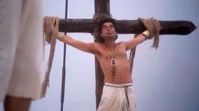 Movie still of crucifixion theme from 'The Life of Brian' where a man is bound to a cross.