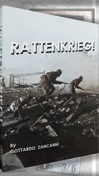 A game box for "RATTENKRIEG!" features a dramatic black-and-white image of two soldiers navigating through a war-torn landscape, emphasizing the game's focus on the Battle of Stalingrad. The title "RATTENKRIEG!" is prominently displayed in bold, white letters at the top, with the designer's name, Gottardo Zancanni, listed below. In the background, various game components, including counters and maps, are partially visible, hinting at the game's intricate mechanics and immersive experience.