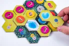 Hexagonal game tiles showing alpine terrain with animals—cheetah, mountain goat, bear, and bighorn sheep—on colored circular tokens. Some tiles feature water, snow, and forest illustrations. Small metal coins with animal icons are placed on tiles.