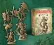 A collection of intricately designed miniatures from the Dragonbane RPG is displayed against a textured green background. The set includes a variety of characters, such as a knight with a spear, a dragon, and a sorcerer, all rendered in a beige color, showcasing their detailed features. To the right, a box labeled "DRAGONBANE DEMONS SET" features artwork of a menacing creature, indicating the theme of the miniatures within the set.