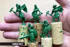 A hand holding several green resin miniatures from the "Ladies Only" collection by Scibor Monstrous Miniatures. The miniatures depict various fantasy female characters, including a warrior with an axe and shield, a knight, and a pirate, all standing on cork bases. The text "Ladies set 2" is displayed at the bottom of the image.