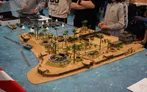 Miniature tropical island battlefield with palm trees, bunkers, tanks, and aircraft on a blue ocean mat.