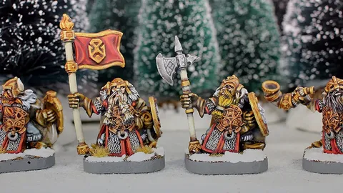 Three painted miniature figures of fantasy dwarves stand on round bases in a snowy outdoor setting with blurred evergreen trees in the background.

The left figure wears a horned helmet, patterned tunic, and fur cloak, holding a pole-mounted red banner with a gold emblem of a snarling face. The figure also carries a round shield on their back.

The center figure, slightly behind the others, wears a helmet with a nose guard, a fur-lined cloak, and carries a pole weapon with a curved blade.

The right figure, holding a large double-bladed axe over one shoulder, wears a horned helmet, fur cloak, and patterned tunic. Their beard is braided and wrapped around their waist.