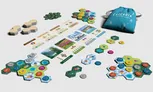 Board game components: hexagonal brown tiles, circular tokens in green, blue, and yellow with icons, rectangular cards showing landscapes, wildlife, and rules, and small metal coins. Some cards display text and images of mountains, forests, and animals.