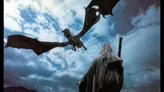 A dragon flying over a hooded figure holding a staff against a cloudy sky.