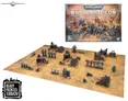 A Warhammer 40,000 tabletop scene with pre-painted plastic terrain. Includes buildings, ruins, and scattered figures in futuristic armor. A rectangular gaming board with a beige surface and printed grid lines. Box cover shows "Warhammer 40,000 Battlefields: Armageddon" with chaotic battle scene.