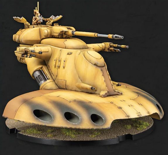 A detailed model of the AAT Trade Federation Battle Tank, featuring a smooth, rounded base with a sandy texture and patches of grass. The tank is primarily yellow, showcasing various weaponry including cannons and missile launchers, with a turret on top that has a small figure positioned in the command seat. The overall design emphasizes a sleek, futuristic aesthetic typical of the Star Wars universe.