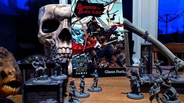 A vibrant tabletop scene features the rulebook for "Boarders and Black Flags" by Man ’o’ Kent Games, prominently displayed in the center. The cover art depicts a dynamic pirate battle on a ship, with characters wielding swords and engaging in combat. Surrounding the book are several unpainted miniatures, including human pirates and undead Skelliwags, set against a backdrop of MDF scenery elements like masts and crates, all arranged on a wooden table.