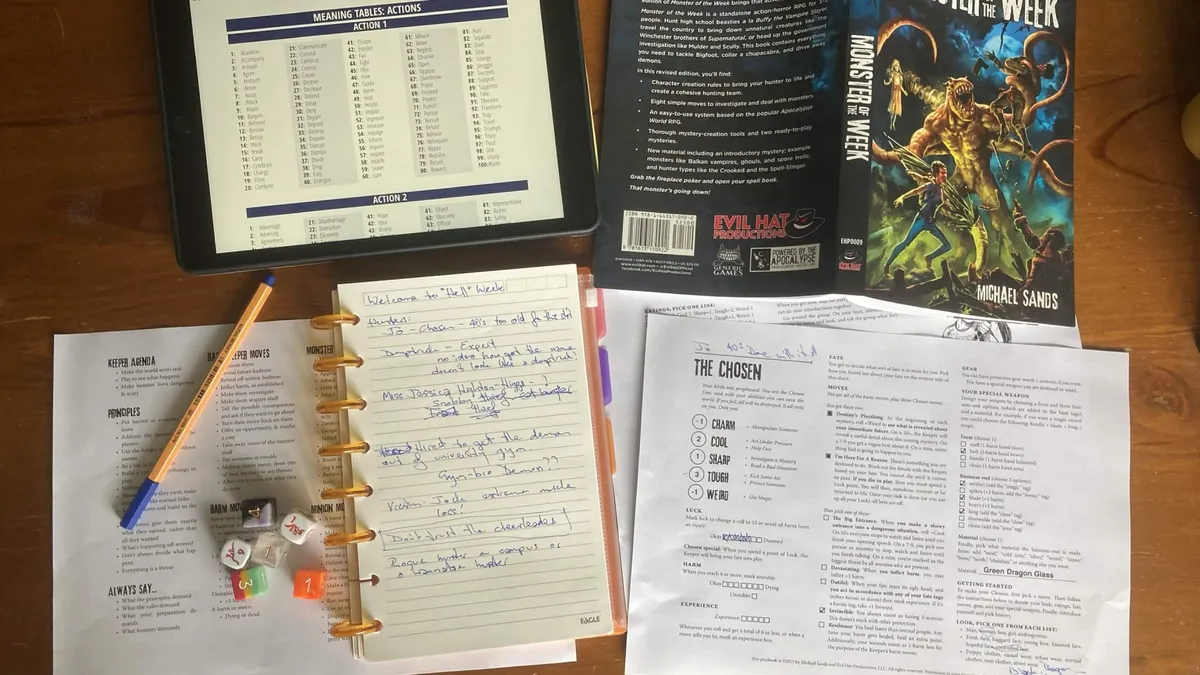 Topdown photo of a solo game in progress. Roll table from Mythic on tablet, Monster of the Week rulebook, journal for note taking, reference sheets