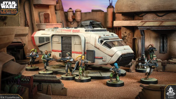 A detailed scene features a Speeder Truck, a large, futuristic vehicle with a sleek design and a prominent red stripe, set against a backdrop of a desert-like environment. Surrounding the truck are five miniature figures, each armed and dressed in varied outfits, including a mix of green and brown tones, suggesting a rugged, adventurous theme. The ground is textured with sandy terrain, and additional elements like crates and structures can be seen in the background, enhancing the immersive atmosphere.
