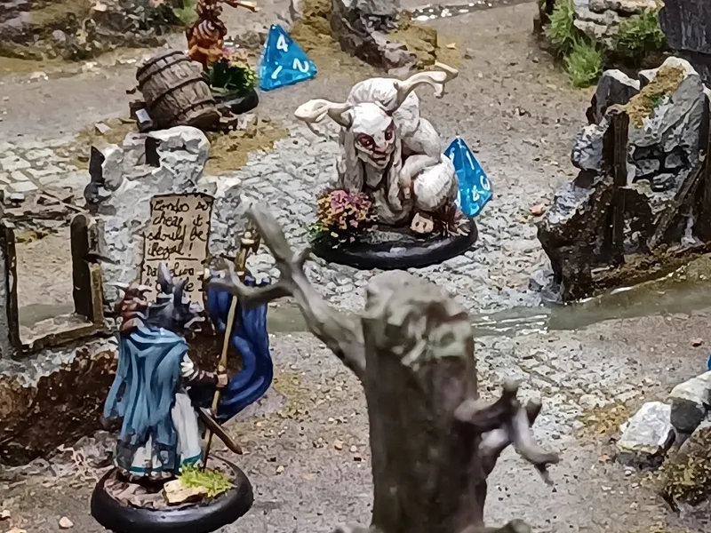 A whimsical scene features a fantastical creature resembling a goat or sheep with large horns, sitting on a rocky terrain adorned with greenery and small flowers. Nearby, a character in a blue cloak holds a sign that reads, "Tendo is cheap and illegal! Not lying!" while another figure stands beside them, holding a sword. Blue dice are scattered throughout the scene, adding to the gaming atmosphere.