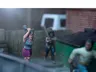 A dynamic scene features three miniature figures in a tense urban setting. In the foreground, a woman with blue hair raises a shovel, while a second figure behind her holds a baseball bat, both appearing ready to confront a threat. A third figure, dressed in a light shirt and blue pants, is seen running away, adding to the sense of urgency in the scene, with a green dumpster and a wooden fence in the background.