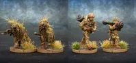 Two detailed miniature soldiers are depicted on circular bases with tufts of grass. The first soldier, on the left, is dressed in camouflage and carries a rifle, while a backpack is slung over his shoulder. The second soldier, on the right, is also in camouflage and is shouldering a weapon system, possibly a missile launcher, with foliage attached for camouflage. The background features a gradient of blue and gray, enhancing the focus on the miniatures.