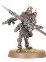 A detailed miniature figure of a Goremonger stands on a textured base adorned with tufts of grass. The figure features a muscular build, wearing a mix of armor and leather, with a menacing mask and spikes on the head. In one hand, it wields a large, jagged weapon, while a firearm is slung across its body, showcasing a gritty, post-apocalyptic aesthetic.