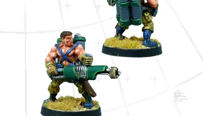 A detailed miniature figure of a commando equipped with a flamethrower, showcasing muscular features and wearing a blue and green outfit. The figure stands on a round base with tufts of grass, and a large backpack containing gas canisters is visible on its back. The image presents the figure from both the front and back, highlighting the flamethrower and the character's rugged design.